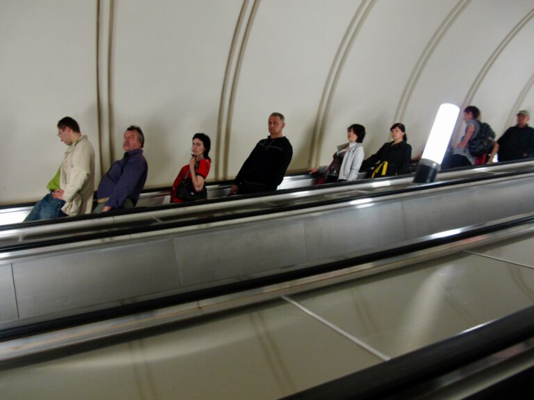 Frau in hellem Mantel fährt auf einer Rolltreppe